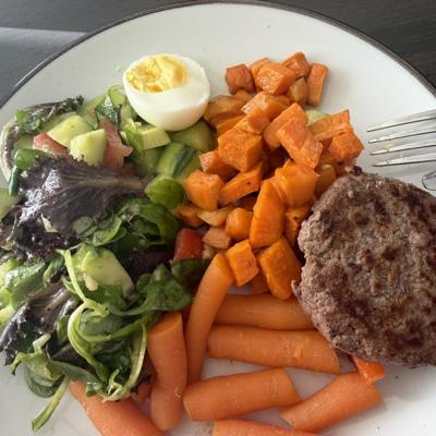 Bord met salade, gekookt ei, zoete aardappel, wortel en een burger