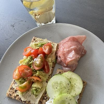 Crackers met avocado, tomaat en hüttenkäse, komkommer en een glas water met citroen