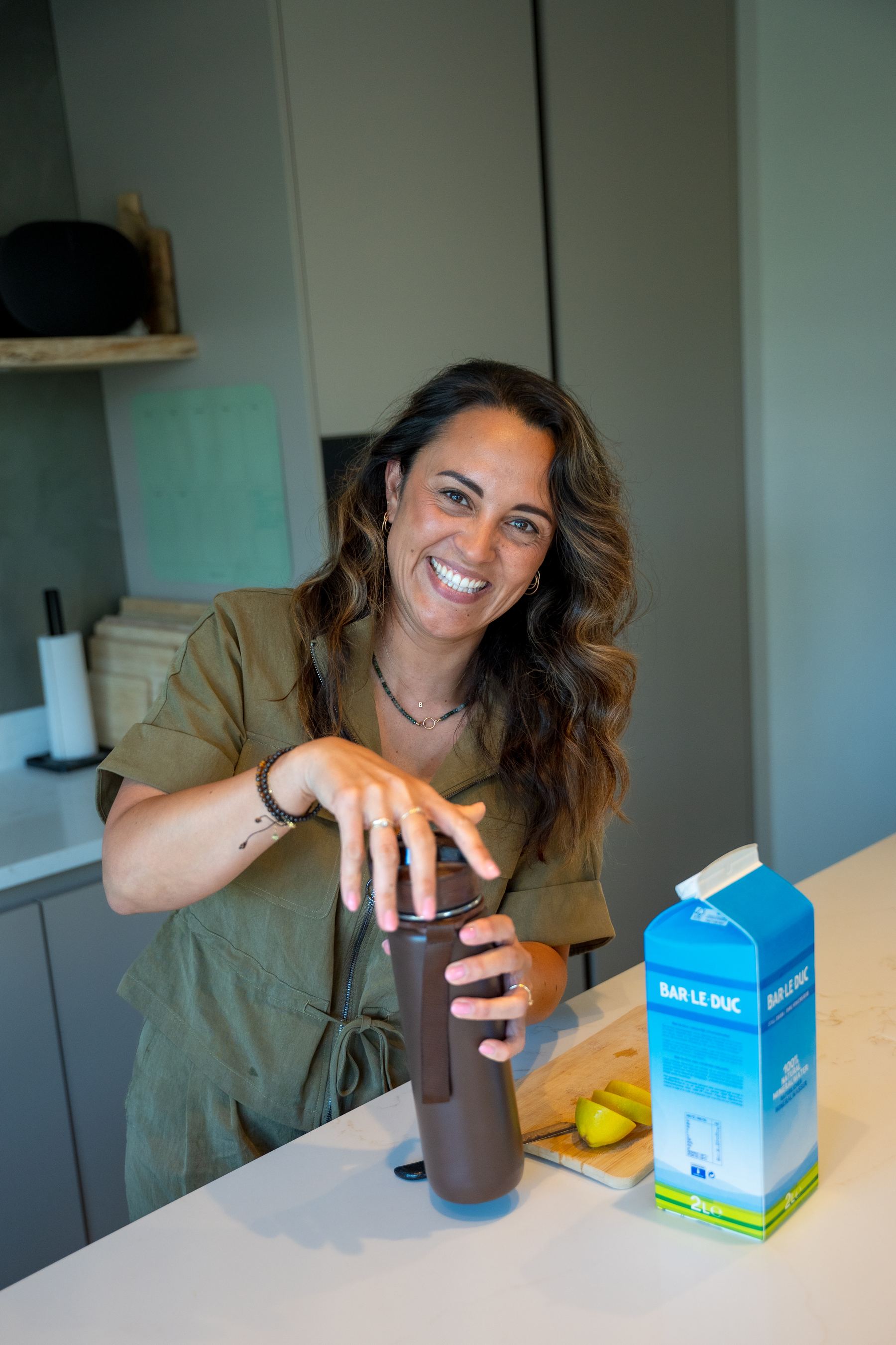 Romy lacht in de keuken met een drinkfles in haar handen